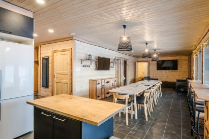Aulanko Lake Villa's main hall. In the foreground, a living room and kitchen corner, in the middle a dining table and a scenery bar counter.