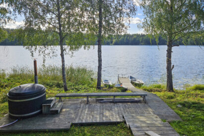 In front of the lakeside sauna of Aulanko Grant Villa, there is a hot tub and a boat dock. The sauna offers a view of the scenic Lake Aulangonjärvi.