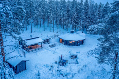 The winter evening darkens at Loppi Wilderness Villa. In the foreground is the accommodation cabin, in the middle the Mini Villa and hot tubs and behind the Main Villa.
